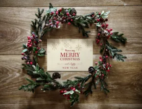 A festive holiday wreath with a 'merry christmas' greeting card mockup on a wooden background. - PSD Mockup
