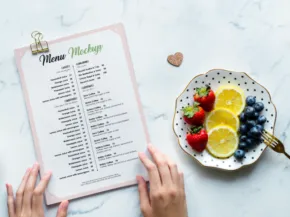 A person reviews a meal planning template next to a plate of strawberries, blueberries, and lemon slices on a marble surface. - PSD Mockup