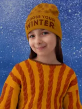 A young girl smiling, wearing a yellow beanie with the text "choose your winter" and a mustard-and-orange striped sweater, against a blue snowy backdrop. - PSD Mockup