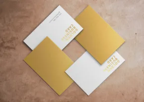 Three gold business card templates on a brown surface. - PSD Mockup