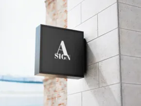 A black square mockup with a white letter "a" logo mounted on a textured beige wall, viewed at an oblique angle. - PSD Mockup
