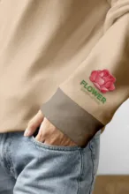A person wearing a beige sweatshirt with a flower patch on the sleeve, tucked casually into denim jeans, serves as an ideal mockup. - PSD Mockup