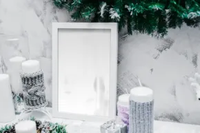 A winter-themed display with a mockup picture frame, white candles, and green garland. - PSD Mockup