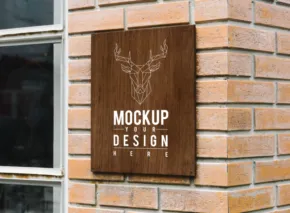 Wooden sign with a stag illustration and text "template" mounted on a brick wall beside a window. - PSD Mockup