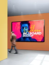 A person walks past a large digital billboard displaying a vibrant template advertisement inside a modern building. - PSD Mockup