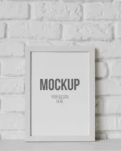 A framed template with the word "mockup" on it, displayed against a white brick wall. - PSD Mockup