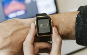 A person checking the time on a smartwatch with a mockup template of a computer screen in the background. - PSD Mockup