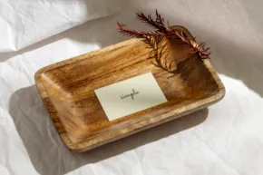 A wooden tray holding a white card with a handwritten word and a dried red flower, placed on a textured mockup. - PSD Mockup