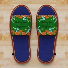 A pair of floral slippers with "wishing you happiness" text on a wooden floor template. - PSD Mockup