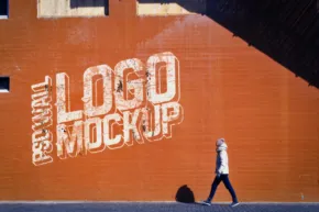 A person walking past a large orange wall with a white "template" spray-painted on it. - PSD Mockup