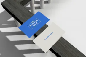 Two business cards, one blue and one white, placed on a textured metallic surface, displaying minimalist and professional design as a mockup. - PSD Mockup