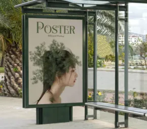 A bus stop with a clear glass shelter, showcasing a template featuring a woman's profile merged with a tree on a tranquil outdoor background. - PSD Mockup