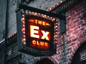 Mockup of an illuminated sign for "the ex club" on a brick wall at night. - PSD Mockup