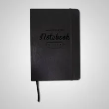 A black notebook with "notebook" embossed on the cover, featuring a bookmark ribbon and a mockup template against a light background. - PSD Mockup