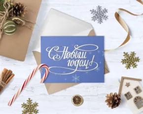 Holiday-themed flat lay template with gifts, a blue card reading "с новым годом", snowflakes, a candy cane, and winter decorations on a wooden surface. - PSD Mockup