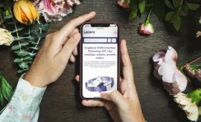 Person using a smartphone mockup to view jewelry amidst a floral backdrop. - PSD Mockup