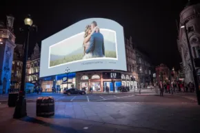 A couple embracing on a large billboard template overlooking a nighttime city street scene. - PSD Mockup
