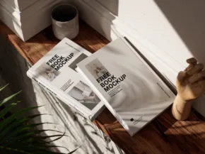 Mockup template displayed in open magazines on a wooden floor near a potted plant, with sunlight casting shadows from a nearby window. - PSD Mockup