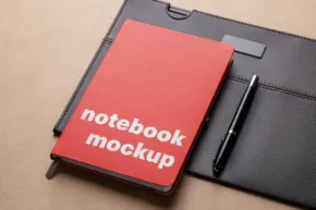 Red notebook labeled "mockup" with a pen on top, lying on a black tablet case against a beige background. - PSD Mockup
