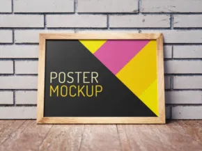 A colorful geometric mockup poster in a wooden frame displayed against a brick wall on a wooden floor. - PSD Mockup