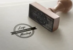 A rubber stamp imprinting a 'logo mockup' design on paper, with the stamp handle held by a hand. - PSD Mockup