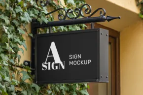 A square sign mockup hanging from a metal bracket with decorative scrollwork, surrounded by lush green foliage. - PSD Mockup