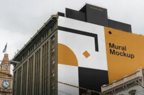 A large mural template in geometric shapes of black, white, and yellow on the side of a city building with cloudy skies above. - PSD Mockup