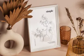 Artistic sketch in a white frame on a beige surface, surrounded by decorative items including a ceramic vase, dried plants, and a textured glass serves as an ideal mockup. - PSD Mockup