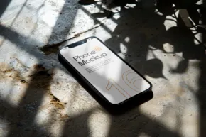 Smartphone with a weather update on the screen lying in dappled sunlight, serving as a mockup. - PSD Mockup