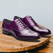 A mockup of shiny purple leather dress shoes with laces on a wooden surface against a neutral background. - PSD Mockup