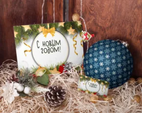 A festive display featuring a sign reading "e. kollim roosom!", a blue ornament, and holiday decorations set against a wooden backdrop, configured as a template. - PSD Mockup