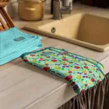 Colorful oven mitt and dish towel on a kitchen counter next to a sink and wooden utensil holder serve as a perfect mockup. - PSD Mockup