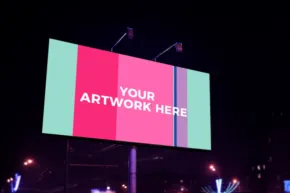 A digital billboard template displaying the text "your artwork here" in a colorful, divided layout, illuminated at night with city lights in the background. - PSD Mockup