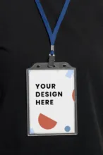 A mockup lanyard with a badge displaying the text "your design here" against an abstract background, worn on a black shirt. - PSD Mockup