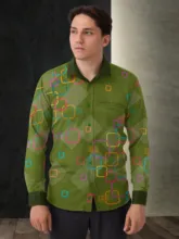 A young man stands looking to his left, wearing a vibrant green shirt patterned with colorful geometric shapes suitable for a mockup template. - PSD Mockup