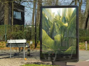 A digital billboard displaying a lush green mockup of plants and flowers, installed beside a park bench and trees on a sunny day. - PSD Mockup
