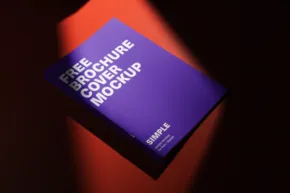 A purple brochure template titled "free brochure cover mockup" resting on a dark surface illuminated by a diagonal beam of orange light. - PSD Mockup