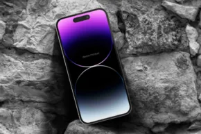 Smartphone mockup with a purple and blue gradient screen resting on a rocky surface. - PSD Mockup