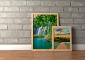 Two framed paintings against a brick wall serve as templates; one depicts a waterfall in a forest, the other a sunset over a field. - PSD Mockup