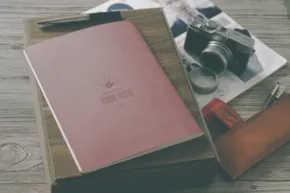A flat lay of a pink journal, camera, photos, and a brown leather case on a wooden table, serving as an ideal mockup. - PSD Mockup