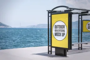 Outdoor bus shelter with advertising templates on a sunny seaside promenade. - PSD Mockup