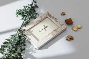 A styled photo of a picture frame with the word "seraphic" displayed, surrounded by green leaves and scattered nuts on a white surface, serving as a mockup. - PSD Mockup