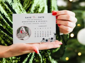 A person holding a "save the date" template for a wedding, featuring a calendar and a photo of a couple, with a Christmas tree in the background. - PSD Mockup