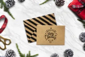 Flat lay template of Christmas gift wrapping essentials with pinecones, greenery, and a stamped envelope. - PSD Mockup