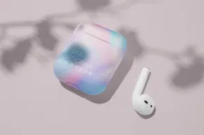 Wireless earbud and its charging case with a colorful design, featuring a template mockup with plant leaves casting a shadow. - PSD Mockup