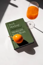 A template with a small orange on top, beside a glass of orange juice with shadows cast by sunlight. - PSD Mockup