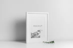 A white book template standing on a plain surface against a light gray background with a small green plant in the foreground. - PSD Mockup