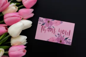 A bouquet of pink and white tulips next to a 'thank you' card on a black background serves as an elegant mockup. - PSD Mockup