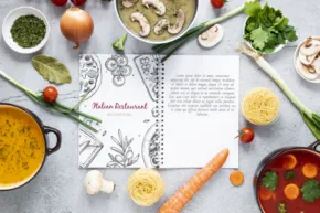 Flat-lay of a variety of fresh ingredients and soup surrounding an open cookbook on a kitchen countertop, serving as an ideal template. - PSD Mockup
