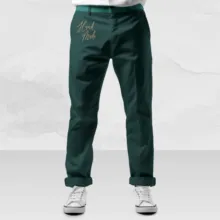 Dark green scrub pants with "val rob" embroidered in gold above the left knee, paired with white sneakers on a grey mockup. - PSD Mockup